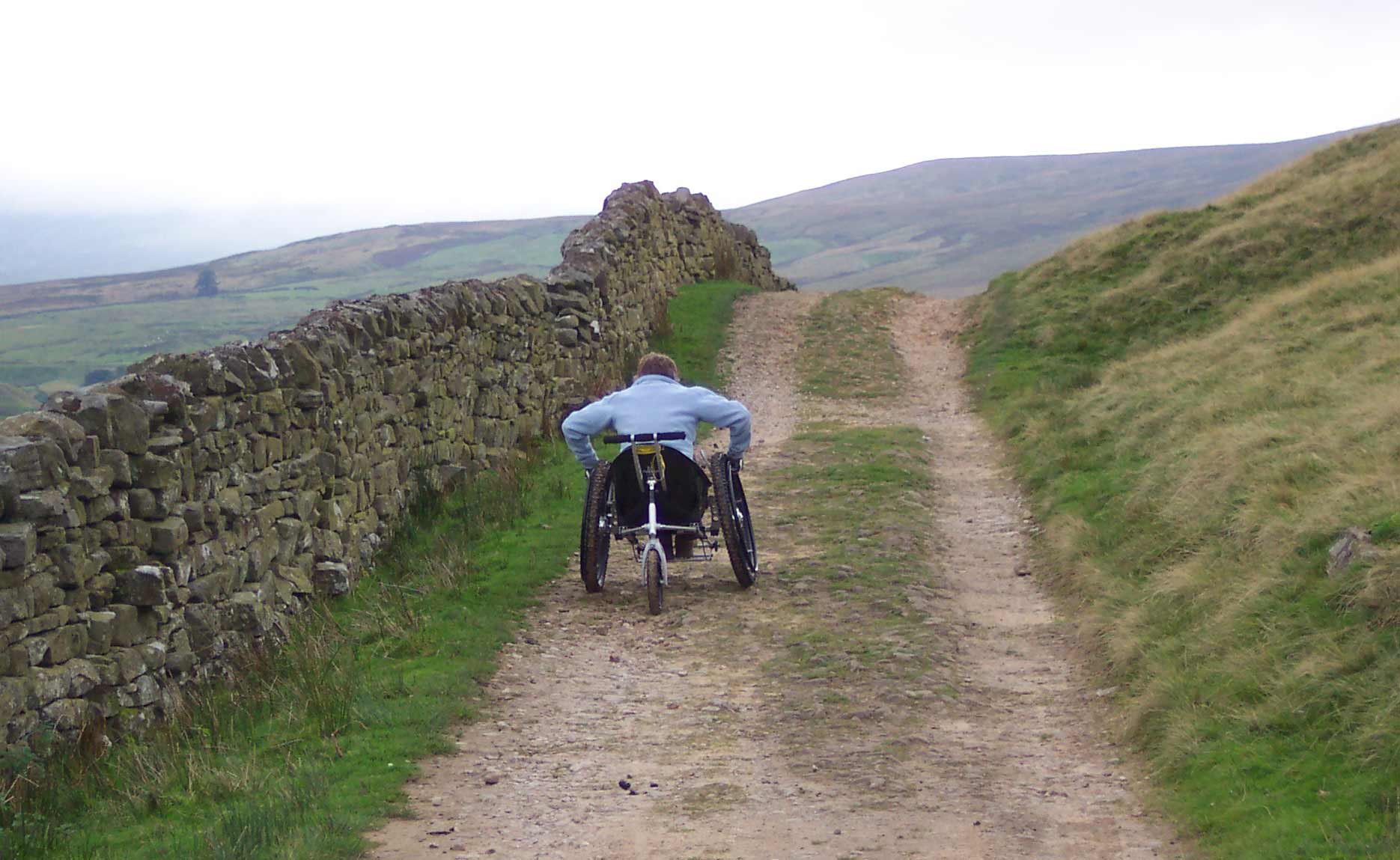 Trekinetic K2 wheelchair user going up rocky trail with hills in background