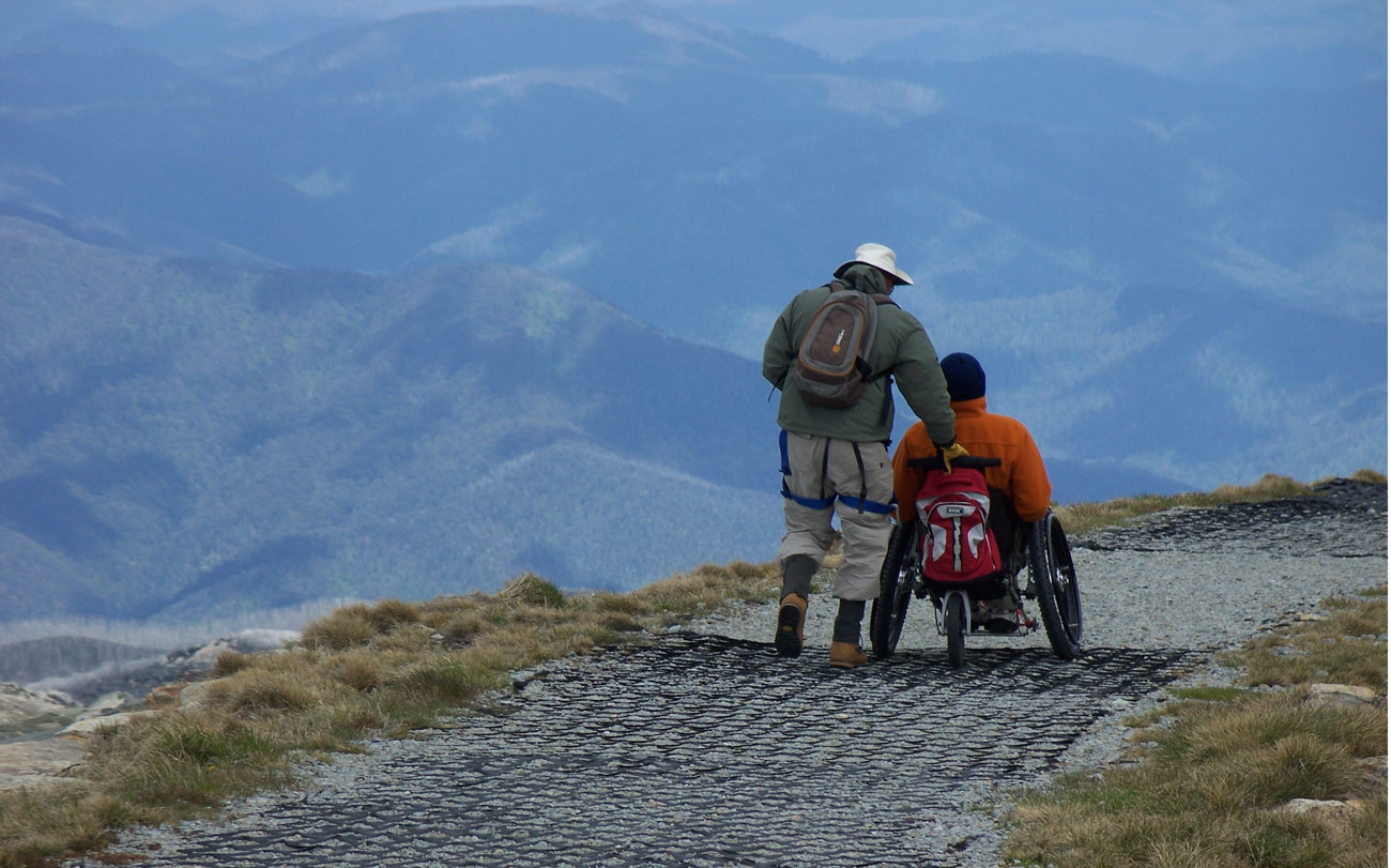 Hiker pushing man in Trekinetic K2 wheelchair on cobbled path up a mountain