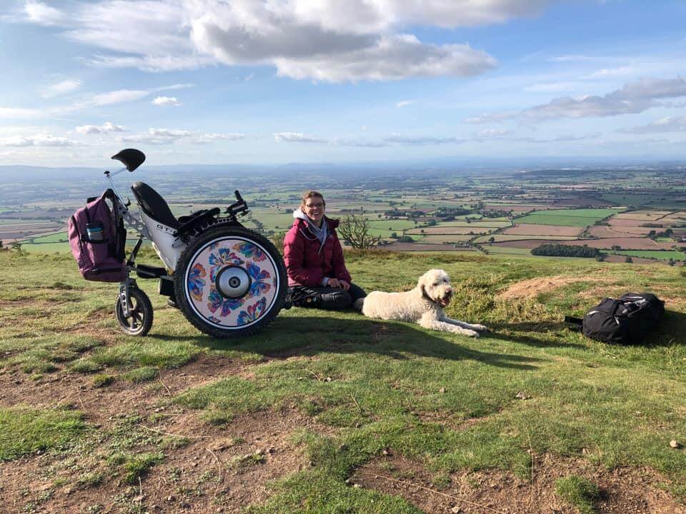 Photo of woman siting on a hillside looking over the view with her dog by her side
