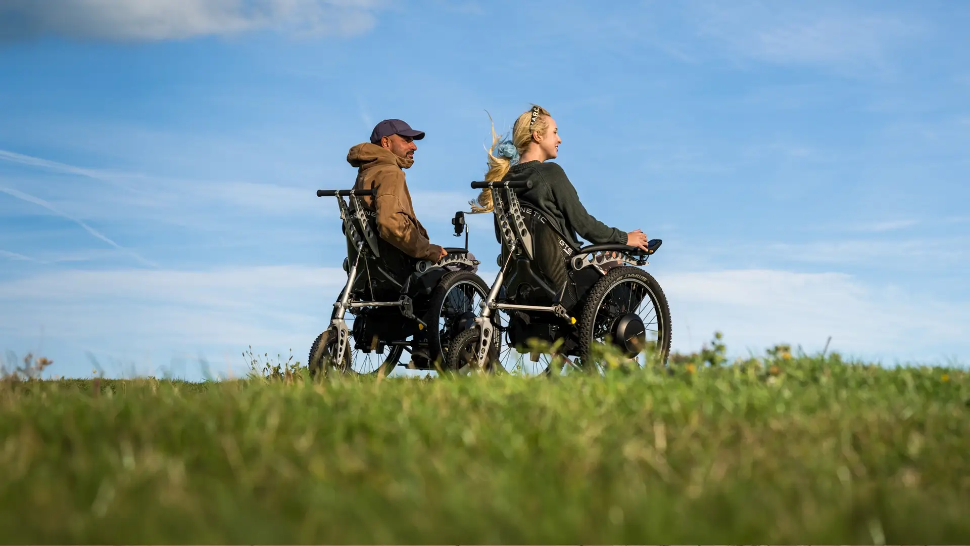Two Trekinetic users side by side on open grassland under a blue sky